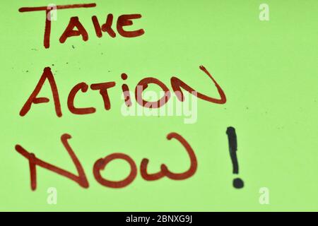 Close up of a fluorescent green color post-it note.The words "Take Action Now" are hand written on capital letters in red marker pen. Stock Photo