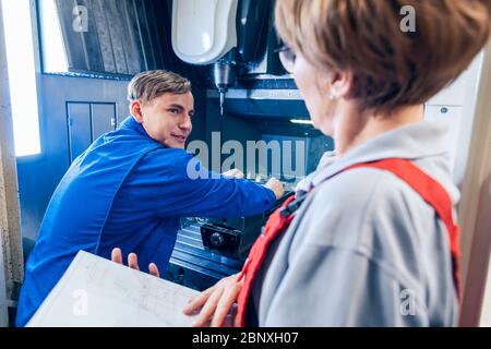 Supervisor watching young worker changing setup of lathe machine Stock Photo