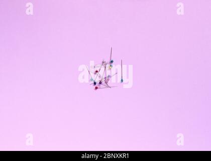 Tailor pins with transparent multi-colored heads lie on a pink background. Stock Photo