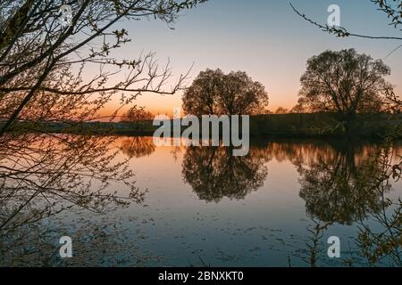 A beautiful orange sunset in the silhouette of trees and bushes on a small lake Stock Photo