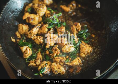Thai basil checken in frying pan, traditional stir-fried meal being cooked, chops of chicken meat with green basil leaf frying close up Stock Photo