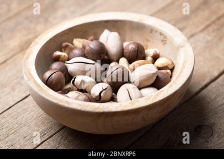 Dried mixed nuts in wooden bowl closeup. Macadamia, Pecan and Brazil nuts with knife on wooden table. Studio macro shoot. Stock Photo