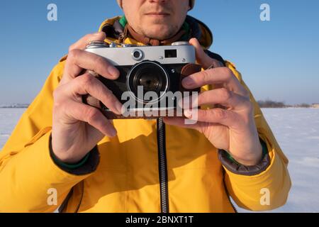 Photographer in yellow jacket taking photo on snowy winter field Stock Photo