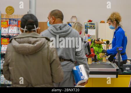 Tuscany, Italy 04/14/20 A cashier at a grocery store wearing coronavirus protection mask and gloves, scanning toilet paper and other products. Shoppin Stock Photo