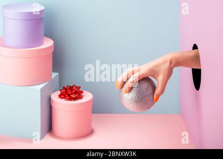 Woman's hand holding a silver ball on blue and pink background Stock Photo