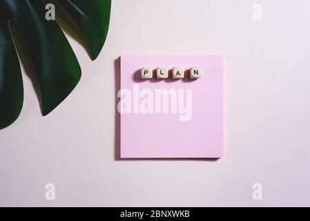 Flat lay of empty blank and wooden bricks with sign Plan on it and partly a leaf of monstera on the pink background. Stock Photo