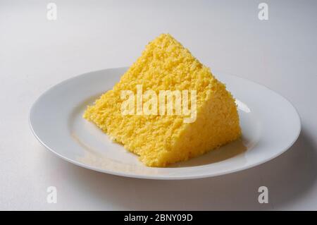 Gastronomy. Slice of the traditional corn couscous from northeastern Brazil, on a white plate organic. Stock Photo