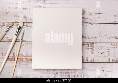 Colorful creative table with blank canvas for sketches and paintbrushes set on white wooden table, top view, copy space, flat lay style, drawing class Stock Photo