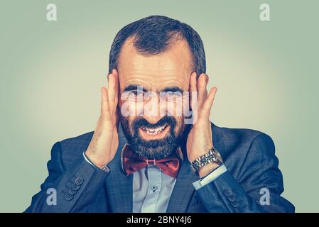 businessman having headache, holding hands on head in frustration, stressed man upset frustrated isolated on light green yellow wall background with y Stock Photo