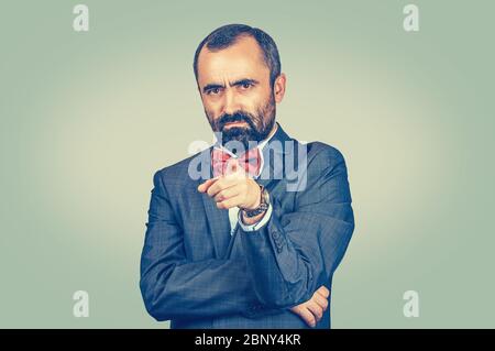 Portrait of a angry young man pointing finger at you camera gesture isolated on light green wall background Stock Photo