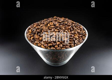 Fresh, roasted coffee beans in a glass bowl, standing on a black table. Stock Photo