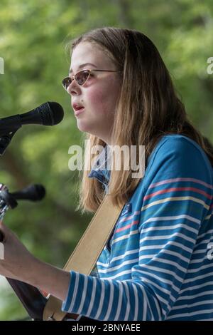 Long haired, teenage girl, with cool sunglasses, playing guitar and singing in band, at oudoor concert Stock Photo