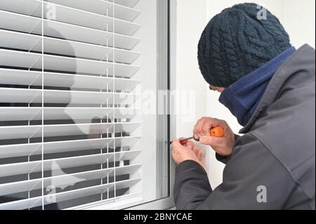 Burglar breaking and entering into home using a screwdriver to open sliding window.