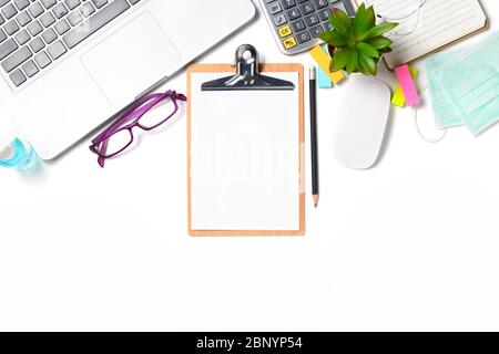 White office desk table blank paper on clipboard and laptop with surgical face mask and sanitizer bottle or alcohol gel with laptop isolated, work fro Stock Photo