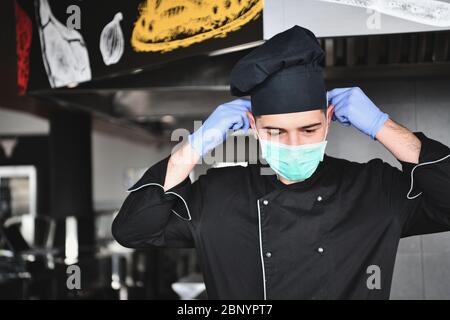 chef cook wearing face protective medical mask for protection from corona virus disease with plate of authentic sandwich at professional restaurant ki Stock Photo