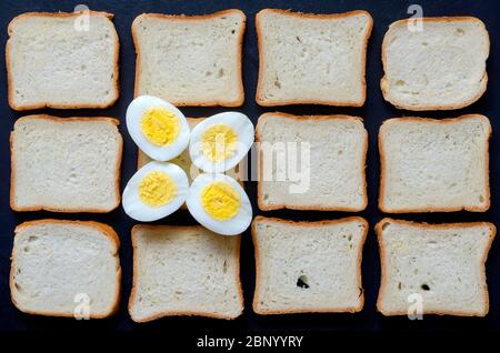 Creative background with boiled eggs and toast bread. Two eggs cut in half on a background of pieces of bread. Multitask background. Place for text. V Stock Photo