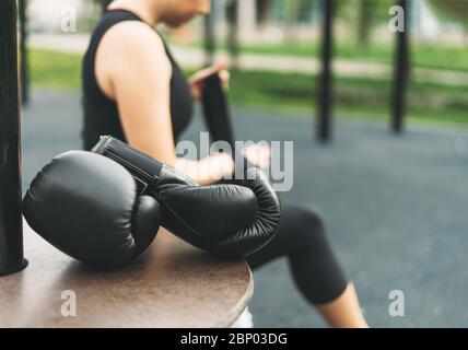 Black leather boxing gloves on background of athletic girl shakes boxing bandages on hands before training Stock Photo