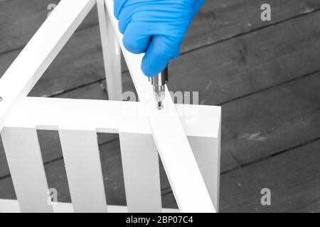 Man assembling a white flat pack ladder shelving unit with a screwdriver.  Flat pack assembly concept Stock Photo