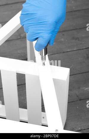 Man assembling a white flat pack ladder shelving unit with a screwdriver.  Flat pack assembly concept Stock Photo
