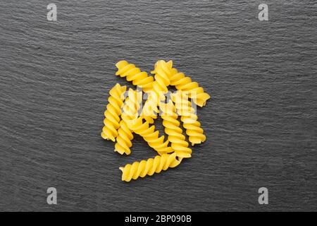 Spiral pasta sprinkled in a heap on a black background. place for text Stock Photo