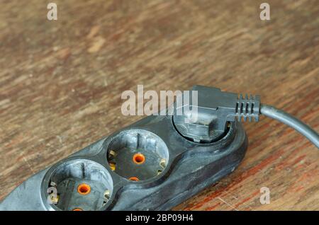 Used electric extension cord on a wooden table. Black developer with a plug in the plug. Electrical Safety Rules. Close-up. Selective focus. Stock Photo