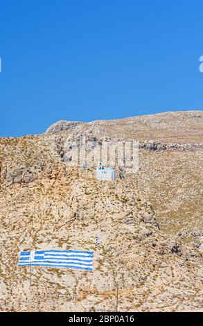 White Greek church and flag of Greece painted on the dry hills of Kalymnos Island, Dodecanese, Greece Stock Photo