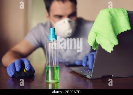 young man wearing medical face mask at work from home office due to corona virus outbreak with laptop on wooden table, remote work against background Stock Photo
