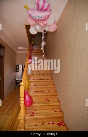 Petals of a red rose on a wooden staircase . Red, yellow, white balloons hanging on the handles of the stairs . Wooden staircase . Stock Photo