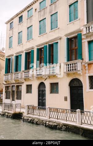 Closeup of the facade of a building, on the streets of Venice, Italy. The four-story building is sand-colored with green forged wooden shutters and Stock Photo