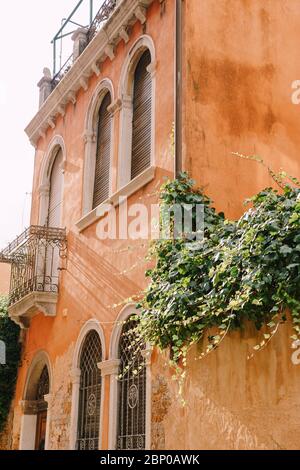 Ancient building in Venice, Italy, close up. Peach-colored walls, classic Venetian arched windows with wooden shutters, small balcony with forged Stock Photo