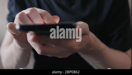 Closeup young man in black t-shirt use smartphone while sitting on a couch Stock Photo