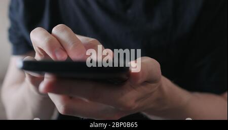 Closeup young man in black t-shirt use smartphone while sitting on a couch Stock Photo