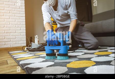 Dry cleaner's man employee removing dirt from carpet, vacuum clean with professional equipment. Stock Photo