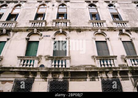 Closeup of the facade of a building, on the streets of Venice, Italy. White stone building with classic arched Venetian windows and wooden shutters. Stock Photo
