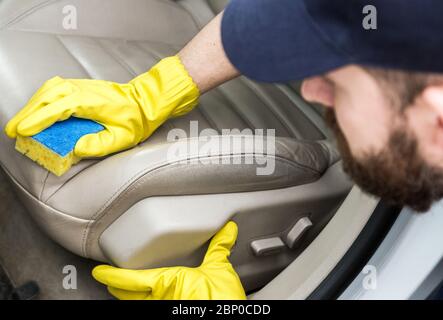 Cleaning service. Man in uniform and yellow gloves washes a car interior in a car wash. Worker washes the chairs of the leather salon Stock Photo