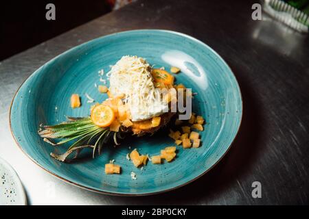 Freshly prepared salad lies inside the pineapple, which is cut lengthwise, sprinkled with grated cheese. Everything looks very appetizing. Stock Photo