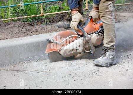 A road service worker using a waste petrol saw cuts the asphalt in a cloud of concrete dust and flying sparks. Stock Photo