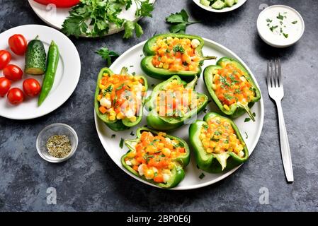 Baked green bell peppers filled with corn, carrot, cauliflower on white plate over blue stone background. Healthy diet or vegetarian food concept. Stock Photo