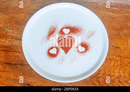 Composition made with red hearts drawn on a white plate from paprika powder on a wooden table Stock Photo