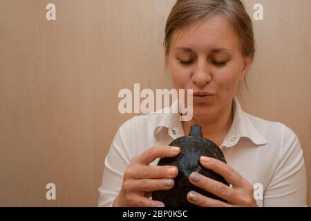Woman holds a turtle in hands. Middle aged white woman shows small tortoise with yellow belly. Care about lovely pet or veterinarian examination Stock Photo