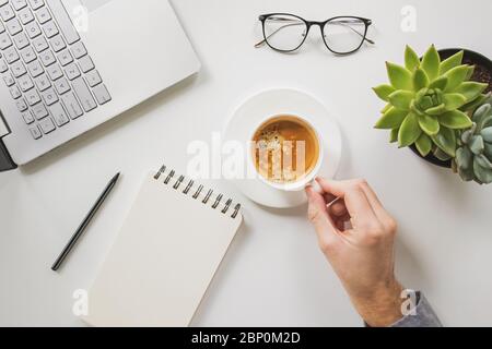 Man's hand holding cup of coffee on his workplace Stock Photo
