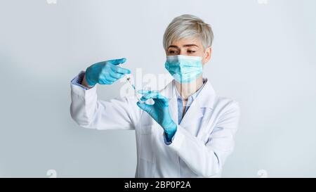 Female doctor in medical mask picks up syringe to give an injection Stock Photo