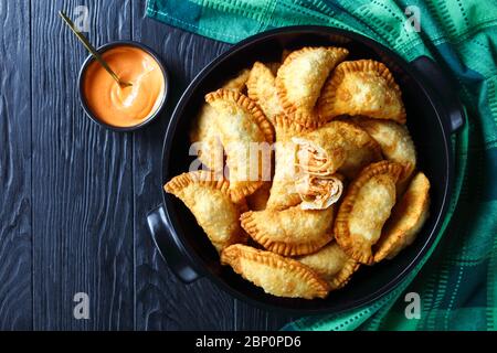 hot juicy Buffalo Chicken Empanadas with Low-Calorie Dip on in a black ceramic pan on a wooden table, horizontal view from above, flat lay, free space Stock Photo