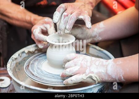 The potter makes pottery dishes on potter's wheel. The sculptor in workshop makes clay product closeup. Hands of the potter. Stock Photo