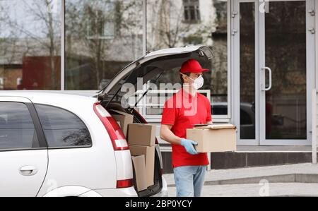 Courier in protective mask and gloves holds box near car at street Stock Photo
