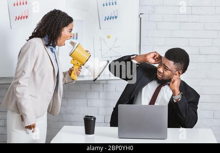 Enraged female boss with loudspeaker yelling at subordinate in company office Stock Photo