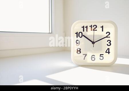 Rectangular white alarm clock on window background. Stock Photo