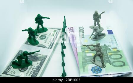 Miniature plastic figure of soldiers on top of two bundles, one made of dollar bills and the other of euros with a plastic ditch in the middle Stock Photo