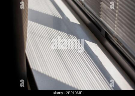 Shadow and light through blinds window on window sill. Morning light and shadow. Curtain on the left. Stock Photo