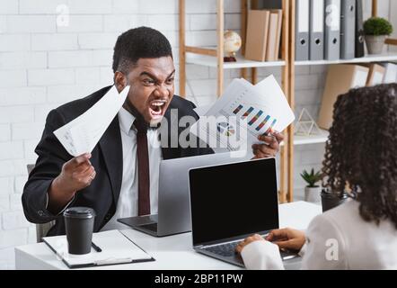 Furious black guy arguing with his female colleague at workplace, empty space Stock Photo